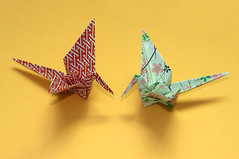 Origami-Kraniche aus einem rotweiß gemusterten und einem grünen, mit rosa und blauen Blüten verzierten Papier